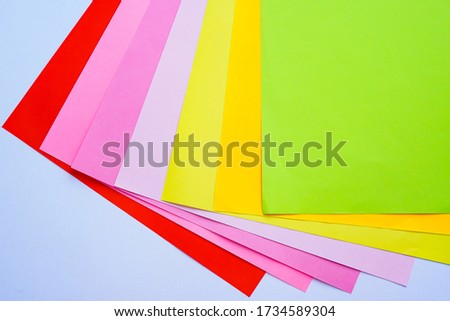Sheets of bright colored office paper are photographed from above close-up on a white background. Red, pink, purple, yellow, orange, green