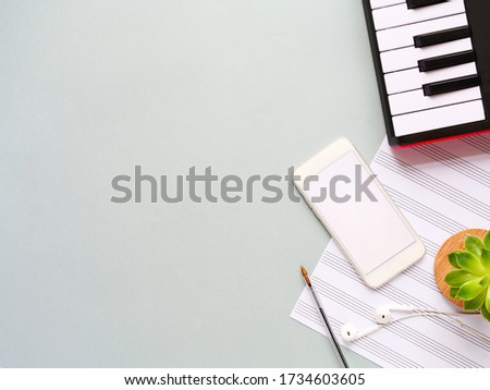 Top view of piano keyboard with sell phone, headphones, note paper and plant on grey background. Study on smartphone, music online lesson, distance learning, hobby, home activity сoncept, copyspace