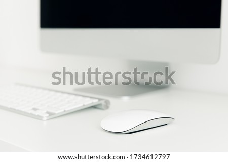 
White computer mouse on desktop close-up, on background of monitor and keyboard. Learning concept. Business style.