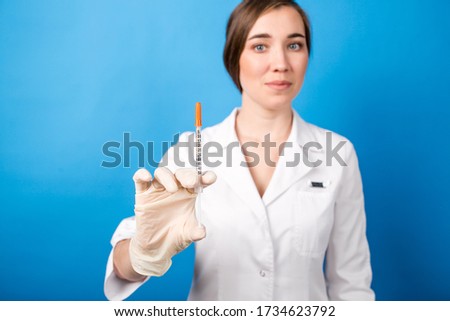 Female doctor holding a syringe with a vaccine in the foreground standing on a blue background