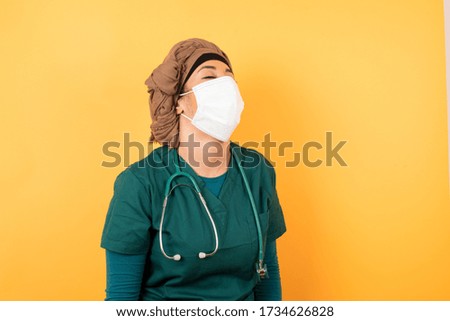 Joyful European doctor woman having fun and laughs at good joke or sings wears casual clothes, standing against gray wall. Happy woman wearing hijab poses indoors.