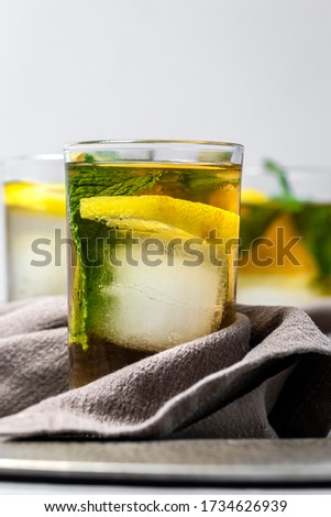Refreshing glasses of tea with ice, mint and lemon wedges on gray table