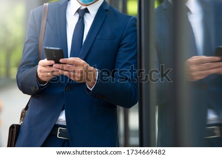 Young businessman with mask using phone outdoor closeup