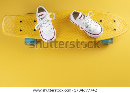Photo of white sneakers on the skateboard or penny board over yellow background.