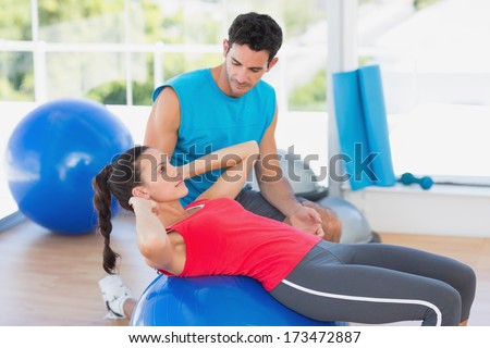Side view of a male trainer helping woman with her exercises at a bright gym