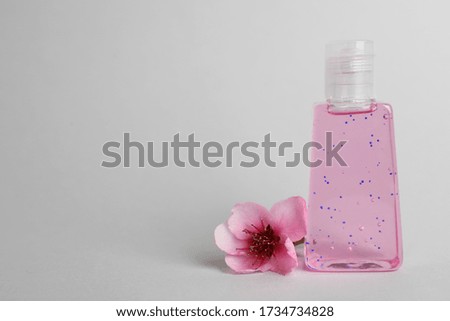 Bottle with antiseptic gel and flower on light grey background, space for text