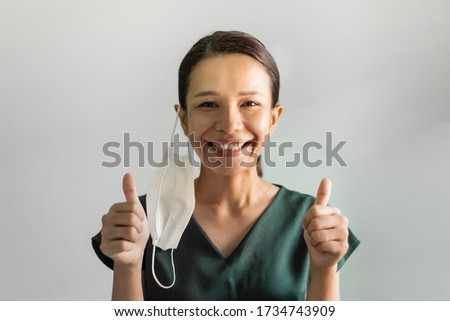 Asian woman feeling happy and showing thumbs up after Coronavirus or Covid-19 crisis is over. Studio portrait Asian woman takes off mask with big smiling and looking at the camera on grey background. 