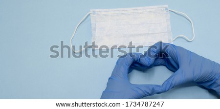 Disposable medical mask and hands in gloves on a blue background. Surgical mask and heart image hands. Save lives from virus, a pandemic. Health protection from coronavirus. Love. Web banner. Isolate