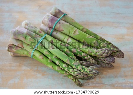 Close up Picture of two bunches of freshly harvested spring green asparagus stalks connected together by elastic rubber band lying on the old vintage wooden table and waiting to be used in kitchen.
