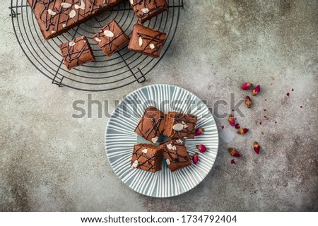 Homemade brownies with almond petals and rosebuds on a textured plate on a wooden background. Top view. Copy space