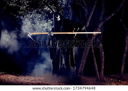 Portrait of grim reaper, the angel of death ( Azrael ) lurking through the woods at night surrounded with mist, smoke in a mystical forest holding his shythe.