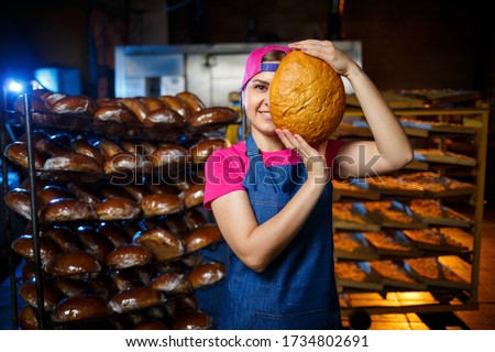 The stage of baking in a bakery. Portrait of a baker girl with bread in her hands against the background of shelving in a bakery. Hands of a baker with bread. Industrial bread production