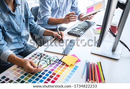 Two colleague creative graphic designer working on color selection and color swatches, drawing on graphics tablet at workplace with work tools and accessories.