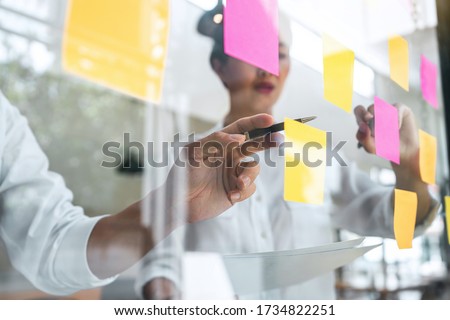 Young creative team professional using post it notes in glass wall to writing strategy business plan to development grow to success. Royalty-Free Stock Photo #1734822251