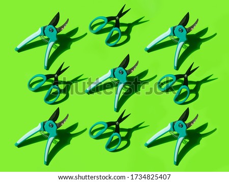 Pattern of secateurs and scissors on a green background with a bright shadow. Garden tools. Creative photo.