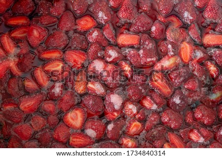 Top view of delicious homemade strawberry jam boiling with sugar and water. Background texture.