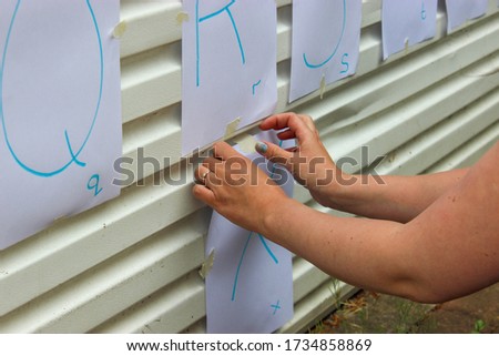 A mother adding hand written letters of the alphabet to a garage door for home schooling during covid-19 