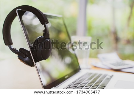 Businessman hanging his modern wireless headphones over the laptop computer screen while taking a break. Setting up working space or home office. Work from home concept with copy space for background. Royalty-Free Stock Photo #1734905477