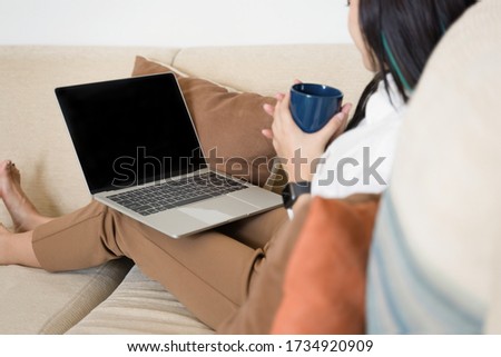 Back view of young female employee in casual wear typing on mockup black screen laptop during working day in home office. Working from home concept