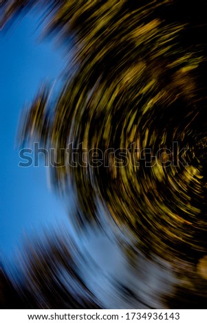 Vortex of yellow green vegetation on clear blue sky - half rotational motion blurred abstract background, texture 