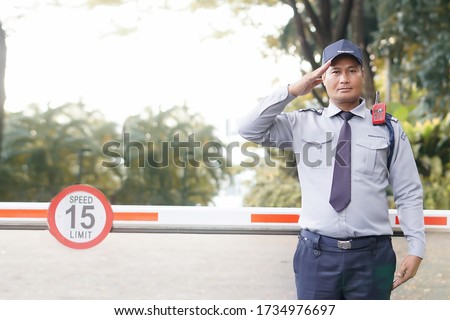 Middle old Asian security guard make saluting entry entrance the village. Security Guard Talking a portable wireless transceiver guard entrance to the village door. Speed 15 limit in area, copy space.
