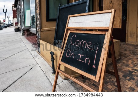Come on in! we're open sign.  Handwritten chalk sign advertising opening back up for business with empty streets, shallow focus on right side of sign