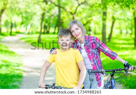 Sporty family leisure. Happy mother embraces her young son, who ride  bikes in a summer park. Empty space for text