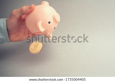 Ethereum selling concept. Piggy bank for coins. Cryptocurrency sell symbol. A man shake out bitcoin from money box on a gray background. Copy space, toned picture