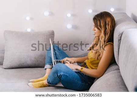Blonde woman working at home with laptop sitting on sofa at home.