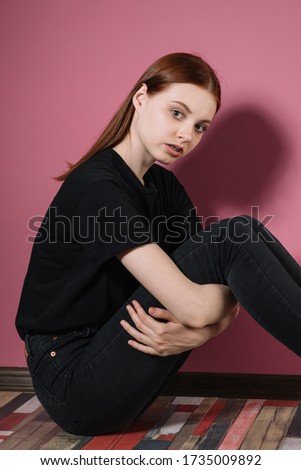 Girl in black poses on a pink background