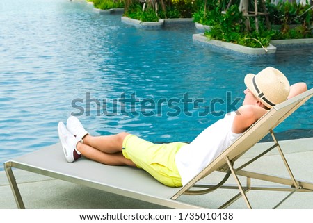 Chaise longue and swimming-pool. Boy on the longue chair near the swimming pool relaxing. Travel concept, travelling, hotel business. Rest, sleep time, relax. Copy space banner.