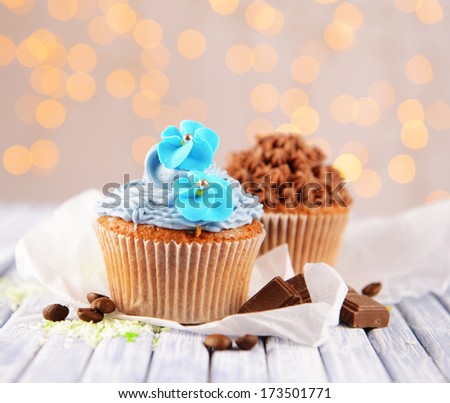 Tasty cupcakes with butter cream, on color wooden table, on lights background