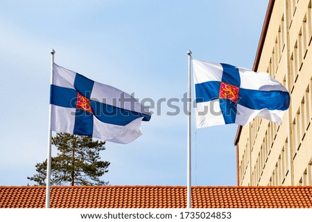 Two finnish national flags with coat of arms on the wind against the blue sky