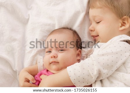 Two children lying on the bed hugging indoors.Older brother laying down ,cuddling ,hugging and holding the hand of his newborn baby brother. Childhood and family concept