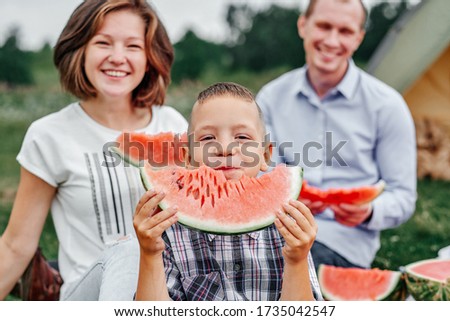 Happy family eating watermelon at picnic in meadow near the tent. Mother, father and child Enjoying Camping Holiday In Countryside.