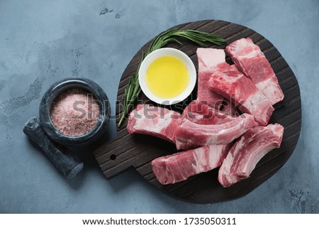 Raw chopped pork ribs with seasonings on a black wooden cutting board, above view on a grey concrete background