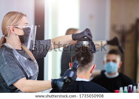A hairdresser with security measures for Covid-19, blow-dry a man in a medicine mask, social distance, cutting hair with a medical mask, eye mask and rubber gloves in a beauty salon Royalty-Free Stock Photo #1735050908