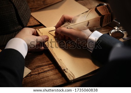 Detective writing with feather on paper at wooden table, closeup