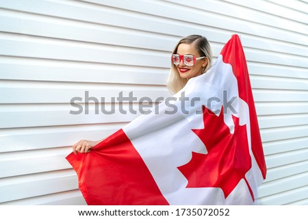 Young beautiful blond hair female person holding national Canadian flag cover her body. Pretty women smiling and holding big Canadian flag and wear sunglasses. Canada Day banner concept. Copy space. Royalty-Free Stock Photo #1735072052