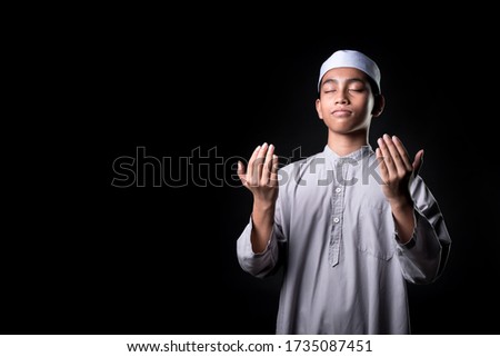Portrait A Muslim boy in Asian Islam is praying for prayer with faith and determination. on black background, with copy space.
