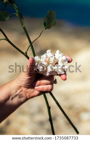 Hand holding white coral with wedding rings and roses. Wedding ceremony on a seacoast in Spain, Mallorca. Concept of marriage, husband and wife, couple, vows, lifestyle,  relationship, love.

