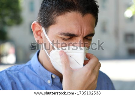 COVID-19 Close up Sick Man with KN95 FFP2 Mask Sneezing or Coughing. Portrait of man with face mask against SARS-CoV-2 sneezing outdoor.
