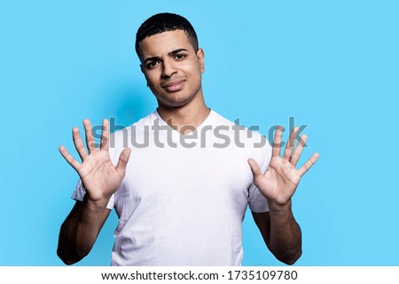 Displeased African American man makes stop gesture with annoying expression, rejects something, clasps palms, isolated over blue background.