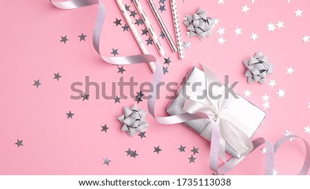 Silver metallic gift box and party decorations with confetti stars on pink background. Festive flat lay composition for girls birthday, Christmas party or wedding