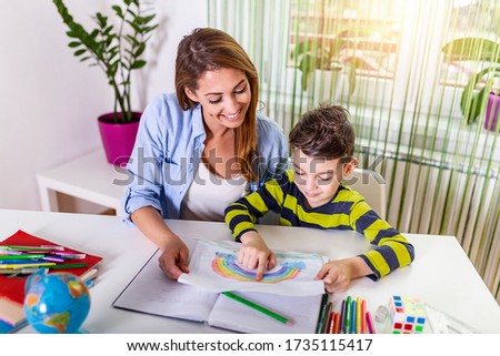 Mom and son are smiling and hugging while doing their homework. Mom helping little boy to do homework. Mom helping kid with homework. Education and family concept