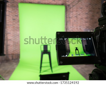 green screen backdrop and black chair with lcd display screen on a High Definition TV camera , 
in studio at TV station. Checking before on air.
