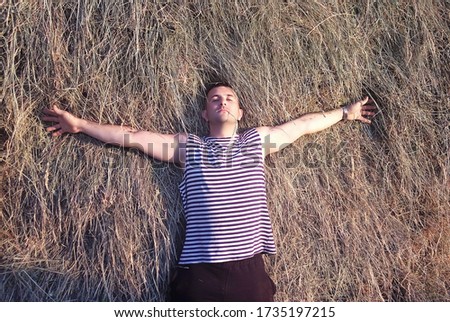 A young man lies in the hayloft with his arms outstretched and resting. View from above.