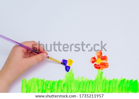 Child's hands drawing flowers on white sheet of paper. Top view.