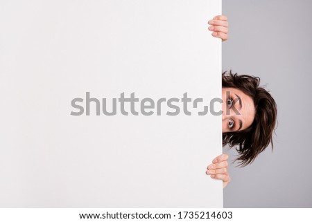 Closeup photo of funny pretty lady holding hands empty paper poster proposing advert place look interested peeking eyes tricky crazy person isolated grey color background Royalty-Free Stock Photo #1735214603
