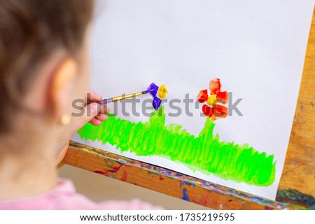 Child's hands drawing flowers on white sheet of paper on an easel.
